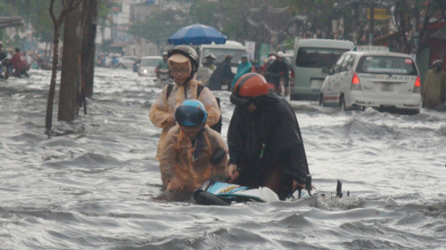 Phần lớn phụ huynh phải tự lo liệu việc đưa đón con đi học. Trong ảnh: Một phụ nữ đón hai con đi học về bị té ngã do mưa ngập trên đường Hòa Bình, Q.11, TP.HCM - Ảnh: Đ.Phú